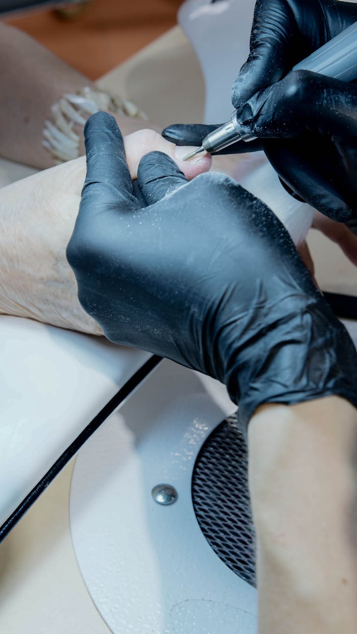 Close-up of a manicurist working on a client's nails using precision tools.