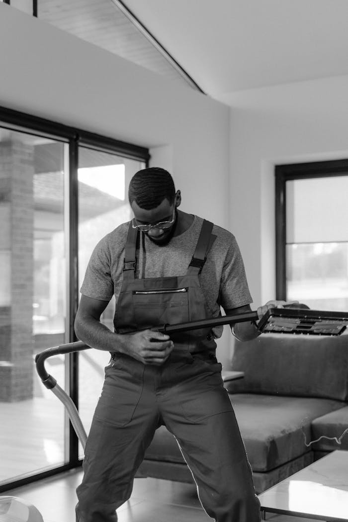 Man wearing overalls cleaning inside a modern home with a vacuum cleaner.